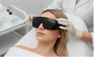 Close-up of a certified aesthetician adjusting protective laser safety goggles on a female patient lying on a treatment bed before starting a facial laser skin therapy session in a medical spa.